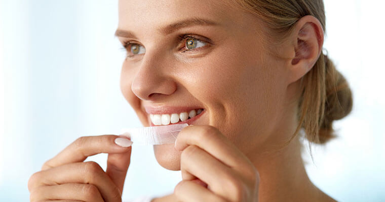 A woman placing a Whitening teeth strip on her teeth